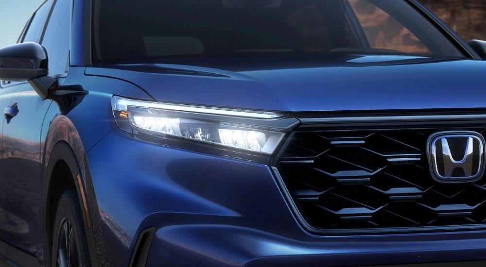 Close-up of the headlight and grille of a blue 2025 Honda CR-V Hybrid for sale.