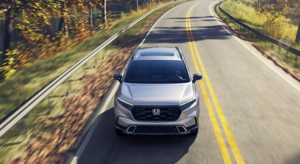 A silver 2026 Honda CR-V Sport Touring Hybrid driving to a Honda dealer near Wheaton.