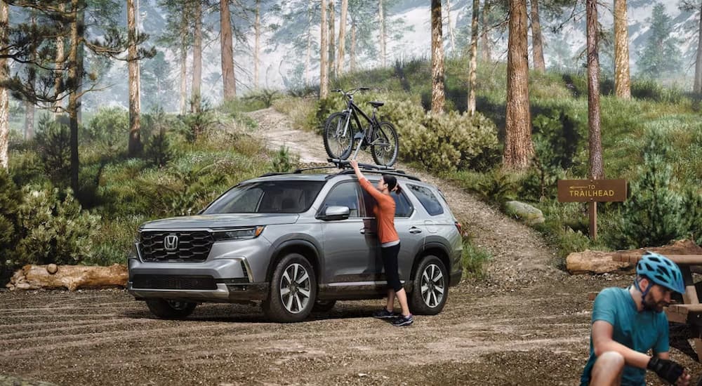 Woman loading bicycle on top of a grey 2025 Honda Pilot Elite.
