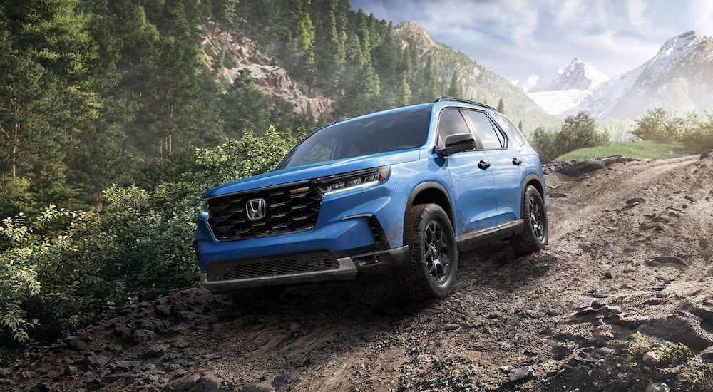 Blue 2025 Honda Pilot TrailSport driving down a dirt hill.