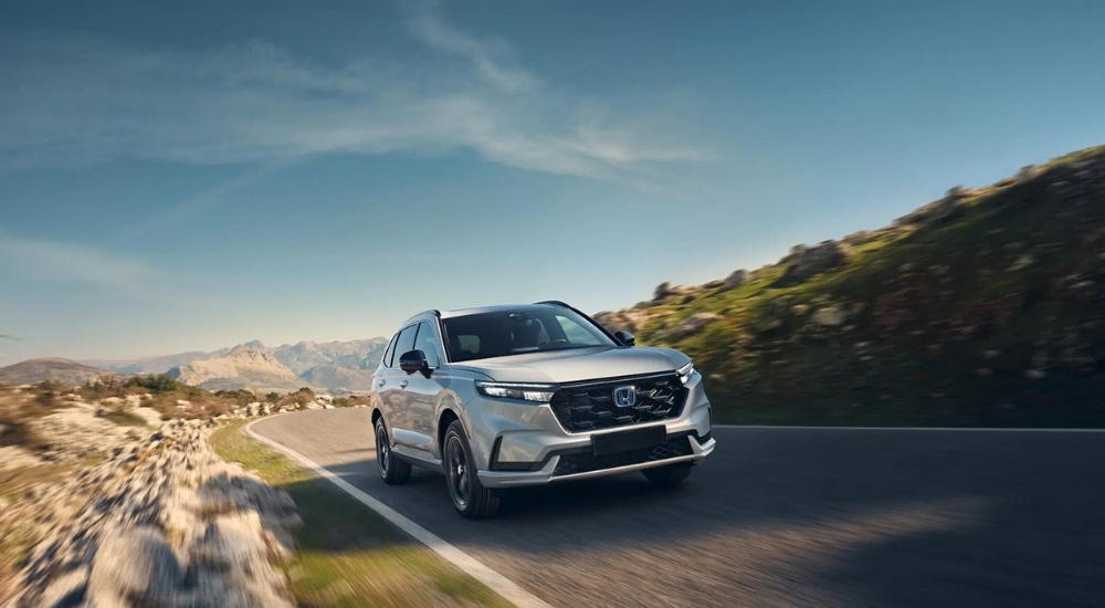 A white 2025 Honda CR-V Hybrid driving down a highway