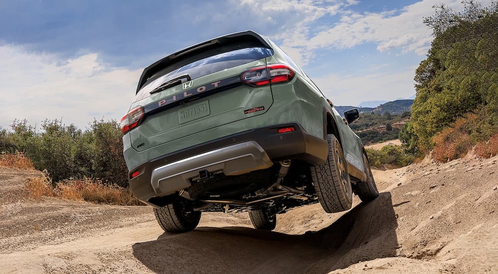 Rear view of a green 2026 Honda Pilot off-roading on a trail