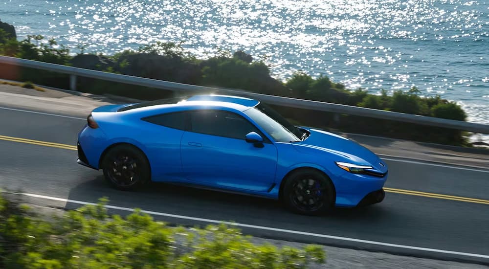 Blue 2026 Honda Prelude driving on a road next to a lake