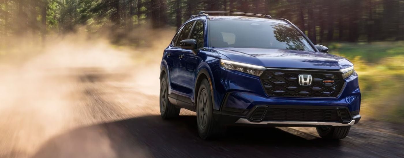 A blue 2026 Honda CR-V hybrid shown speeding on a dirt road.