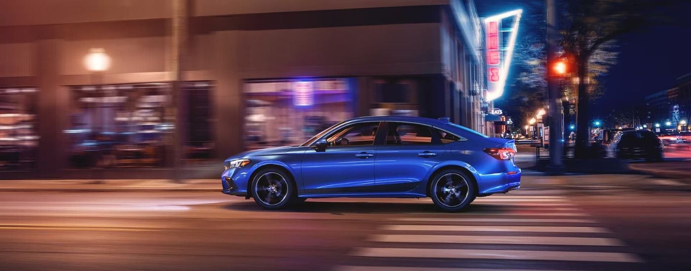 A blue 2023 Honda Civic Touring driving past neon city lights at night.