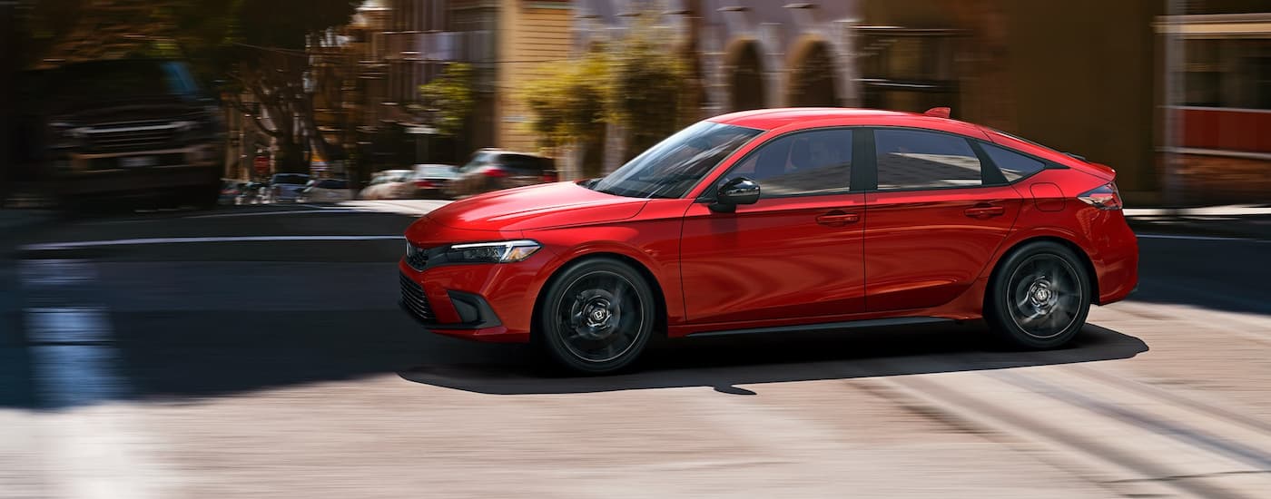 Side view of a red 2022 Honda Civic Hatchback driving through the city.