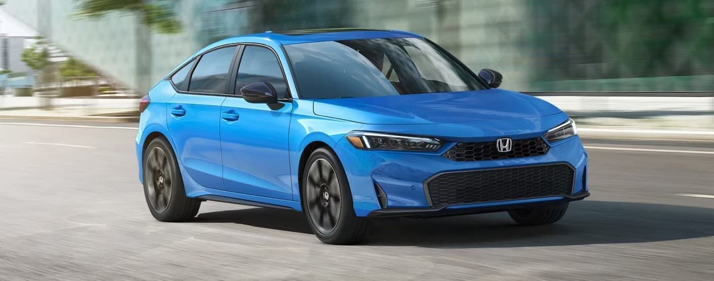 A blue 2025 Honda Civic Hatchback Sport Touring driving in a city.